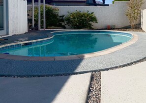 Une piscine à bord incurvé, entourée d’une terrasse en béton et bordée d’un petit muret en pierre.