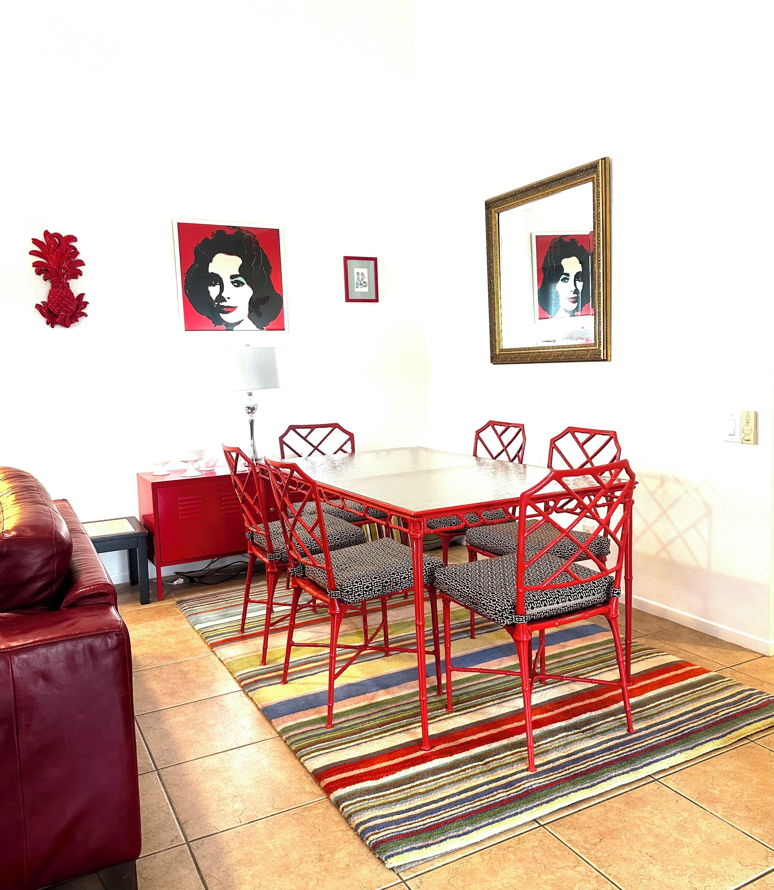 Un comedor con una mesa y sillas de metal rojo, un tapete a rayas y cuadros en la pared.