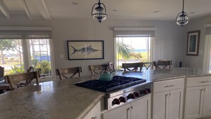 Una cocina con armarios blancos, encimera de granito, hervidor azul y un ventanal con vistas al exterior.
