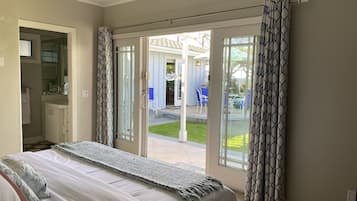 A bedroom with a bed, a bathroom with a sink and mirror, and a sliding glass door leading to an outdoor patio with chairs and a table.