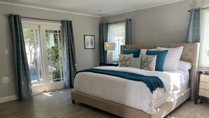 Un dormitorio con una cama grande, una mesita de noche, una lámpara y vista a una piscina a través de puertas corredizas de vidrio.