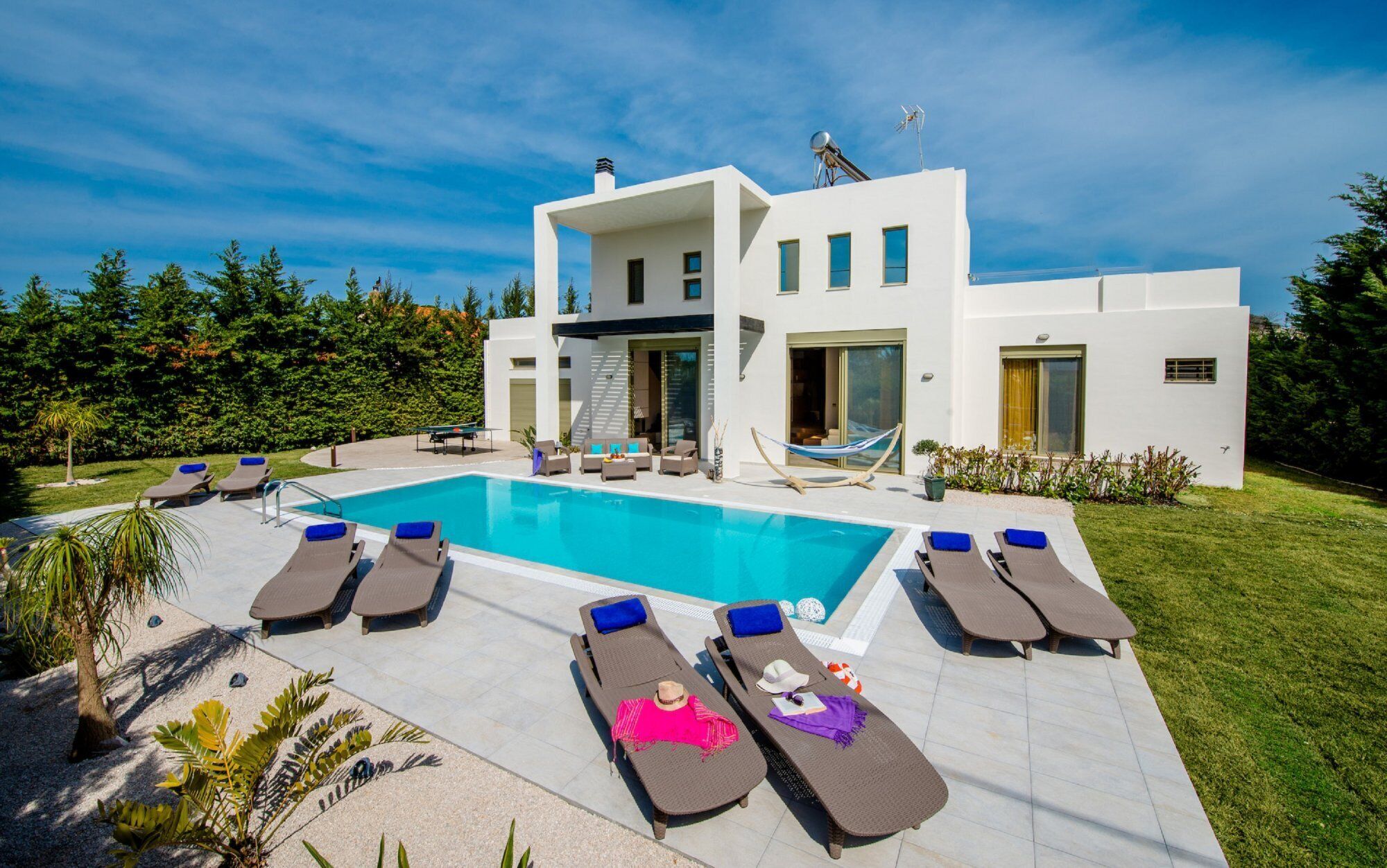 Une maison moderne à deux étages, dotée d’une piscine, de chaises longues et d’un hamac.