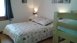 Un dormitorio con una cama, una lámpara de noche, una ventana con cortinas y una pared decorada con dos cuadros.