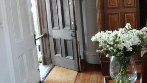 Una habitación con puerta de madera, puerta blanca, un armario de madera y un florero con flores.