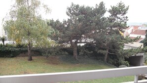 Un balcon donnant sur un espace verdoyant, des arbres et un bâtiment situé au loin.