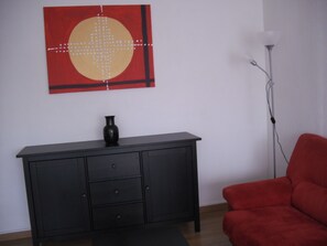 A room with a black cabinet, a red chair, and a painting on the wall.