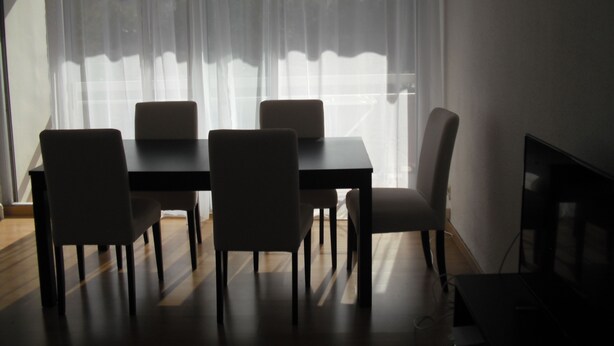 Un coin repas avec une table et des chaises, un téléviseur et une fenêtre agrémentée de rideaux légers.