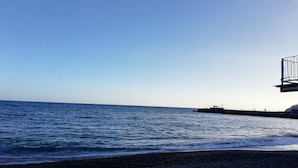 Una playa con costa rocosa y un muelle que se adentra en el agua.