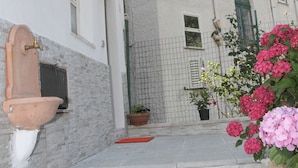 Un edificio con fachada de piedra, una escalinata de piedra que conduce a una puerta y una jardinera con flores rosas.