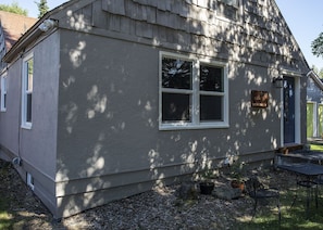 A single-story house with a shingled roof, a front door, and a small porch with a table and chairs.