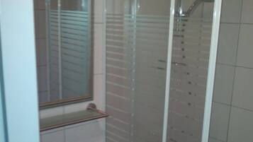 A bathroom with a glass-enclosed shower, a sink with a mirror above it, and tiled walls.