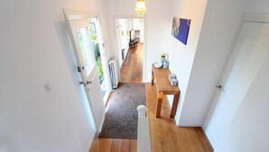 Un pasillo con suelo de madera, una puerta blanca y vistas a una sala de estar con televisor y mesa de comedor.
