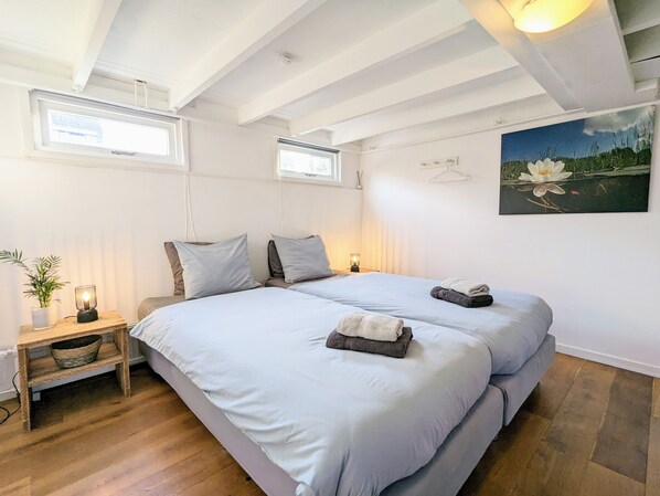 Un dormitorio con una cama grande, mesitas de noche, una planta pequeña y un cuadro en la pared.