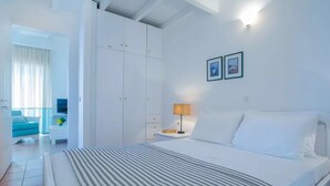 A hotel room with a bed, a bedside table with a lamp, a wardrobe, and a balcony with a chair. - 2 Bedroom Residence Sea View (Paxoi)