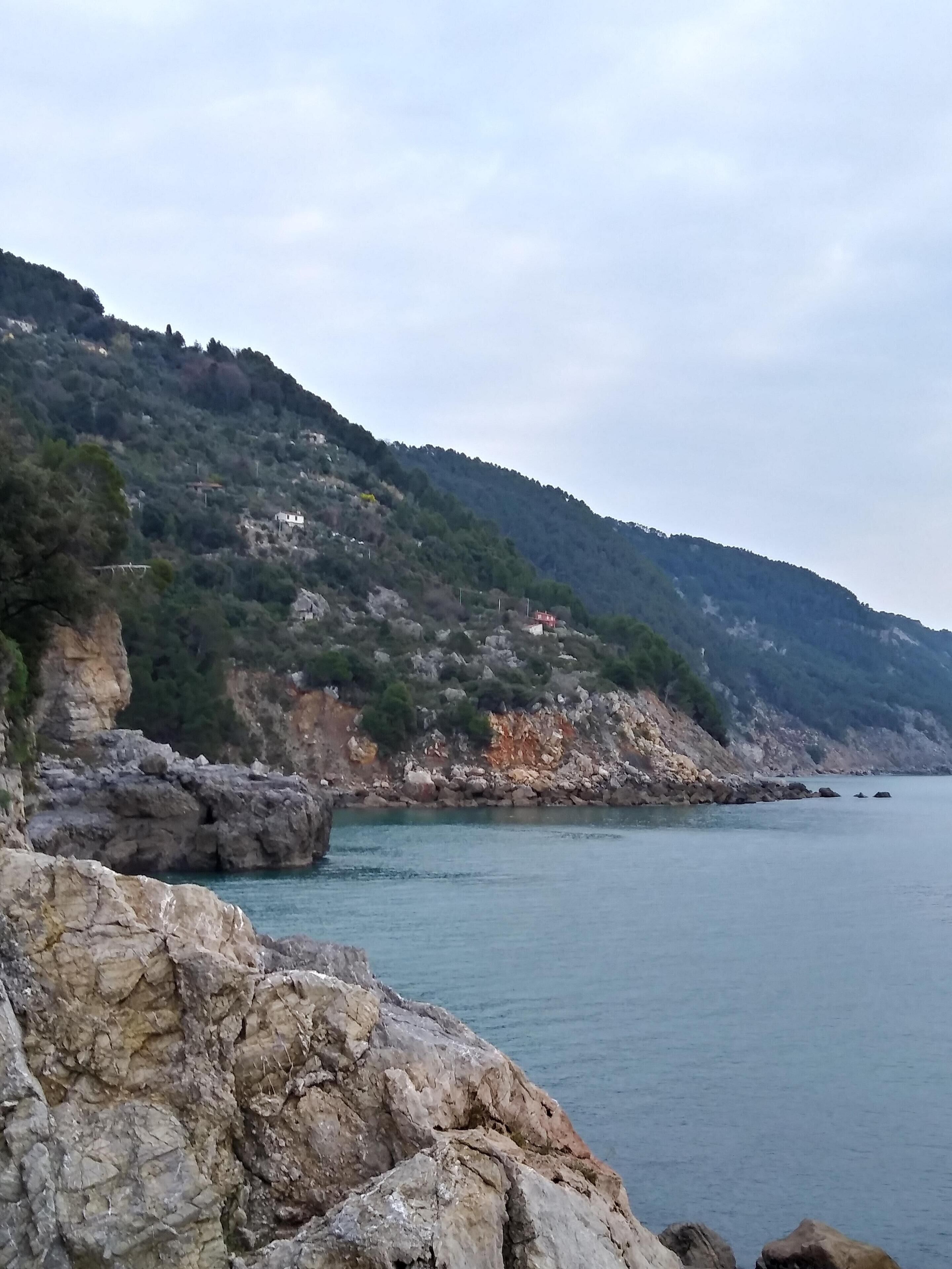 Paisagem costeira com falésias rochosas, mar calmo e alguns edifícios na encosta.