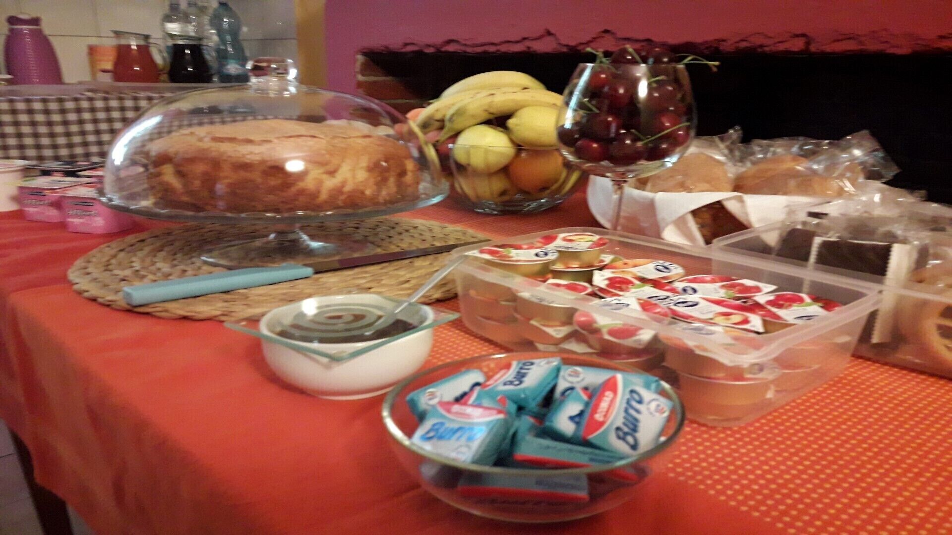 Ein Tisch mit verschiedenen Speisen, darunter eine Kuchengebäck, Bananen, Trauben und verpackten Snacks.