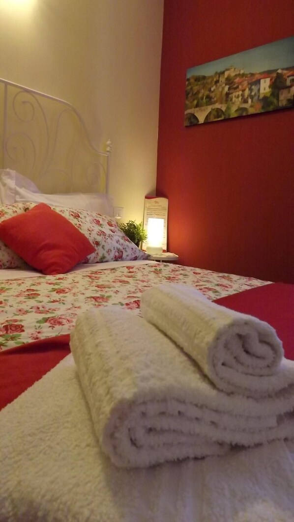 Restful retreat with a floral-patterned bedspread and a cozy red pillow, complemented by a framed picture above the bed.