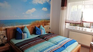 Een slaapkamer met een strandmuur, een bed met gestreept beddengoed, en een raam met uitzicht op de omgeving.
