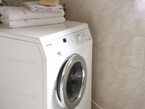 Een voorlader wasmachine, wit van kleur, met een bedieningspaneel en een stapel gevouwen handdoeken erop.
