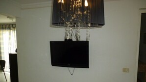 A room with a mounted television on the wall, a chandelier, and a door leading to another room. - Apartment Frida (Los Cristianos)