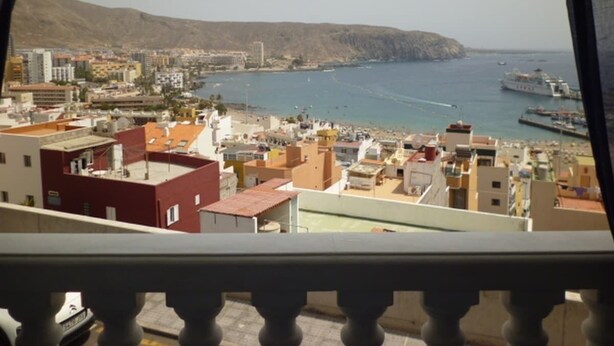 A coastal cityscape with buildings, a beach, and a mountainous backdrop. - Apartment Frida (Los Cristianos)