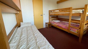 A room with bunk beds and a single bed. There is a door and a small table.
