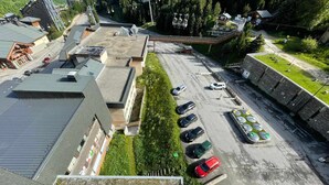 An aerial view of a parking lot with several cars, a small building, and a green area with a fence.