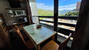 A small kitchen with a table and chairs, a microwave, and a window with a view of mountains and buildings.