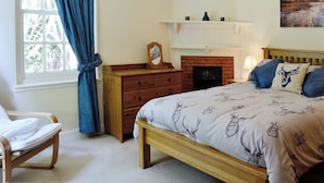 A bedroom with a bed, a dresser, a chair, a fireplace, and a window with curtains.