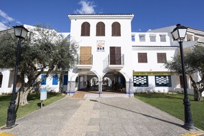 Un edificio blanco con tres ventanales arqueados y un balcón, rodeado de árboles y un cielo despejado.