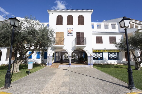 Un edificio blanco con tres ventanales arqueados y un balcón, rodeado de árboles y un cielo despejado.