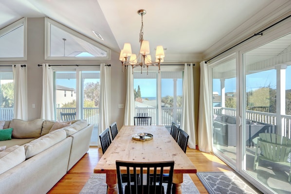 A dining area with a wooden table, black chairs, a chandelier, and large windows offering a view of the outdoors.