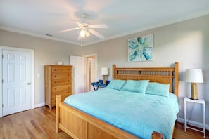 A bedroom with a wooden bed, a ceiling fan, a dresser, and a bedside table with a lamp.