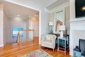 A living room with hardwood flooring, a white armchair, a blue lamp, a fireplace, and a painting on the wall.