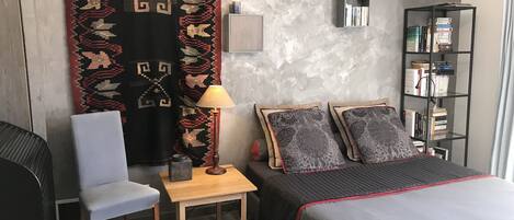 Ein Hotelzimmer mit einem Bett, einem Sessel, einem kleinen Tisch mit Lampe, einem Bücherregal und einem großen Teppich.