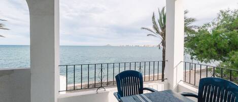 Ein Balkon mit Tisch und Stühlen, der auf eine Küstenlandschaft mit Geländer und Palmen blickt.