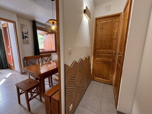 A dining area with a wooden table and chairs, a hanging light fixture, and a wooden door with a geometric pattern.