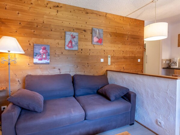 A cozy room with a wooden wall, a sofa, a lamp, and a coffee maker.
