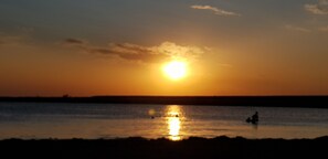 Un coucher de soleil sur une étendue d’eau calme, avec les silhouettes de personnes et d’un bateau.