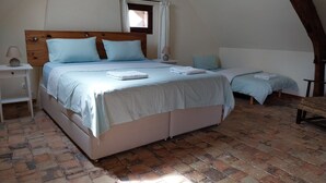 Une chambre à coucher avec un grand lit, un plus petit lit, une table de chevet, une lampe et une fenêtre avec des rideaux.