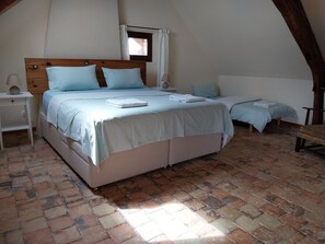 Um quarto com uma cama grande, uma cama menor, uma mesa de cabeceira, uma luminária e uma janela com cortinas.