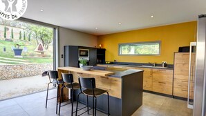 A modern kitchen with a large island, bar stools, and a view of the garden. - Charming Cottage for 6, Private Garden & Pond (Montbrison)