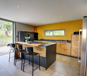 Une cuisine moderne dotée d’un grand îlot central, de tabourets de bar et offrant une vue sur le jardin.