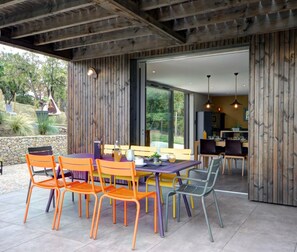 Une terrasse extérieure avec une table et des chaises en bois, un mur en pierre et une vue sur un jardin.