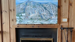 Un mur en bois orné d’une carte encadrée du domaine skiable d’Okemo Mountain, avec une cheminée en dessous et une lanterne au-dessus.