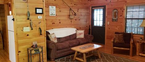 A cozy cabin interior with a wooden interior, a brown sofa, a small table, and a refrigerator.