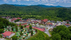 A town with a golf course, buildings with red roofs, and a mountainous backdrop.
