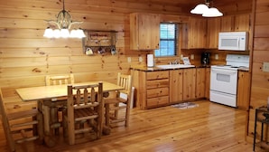 A wooden cabin interior with a dining table, chairs, a kitchen area including a stove, microwave, and cabinets.