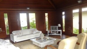 A wooden interior with a white sofa, a coffee table, and a television on a stand. - Villa Cascais - Luxury villa in gated community. Guarajuba/Itacimirim (Guarajuba)