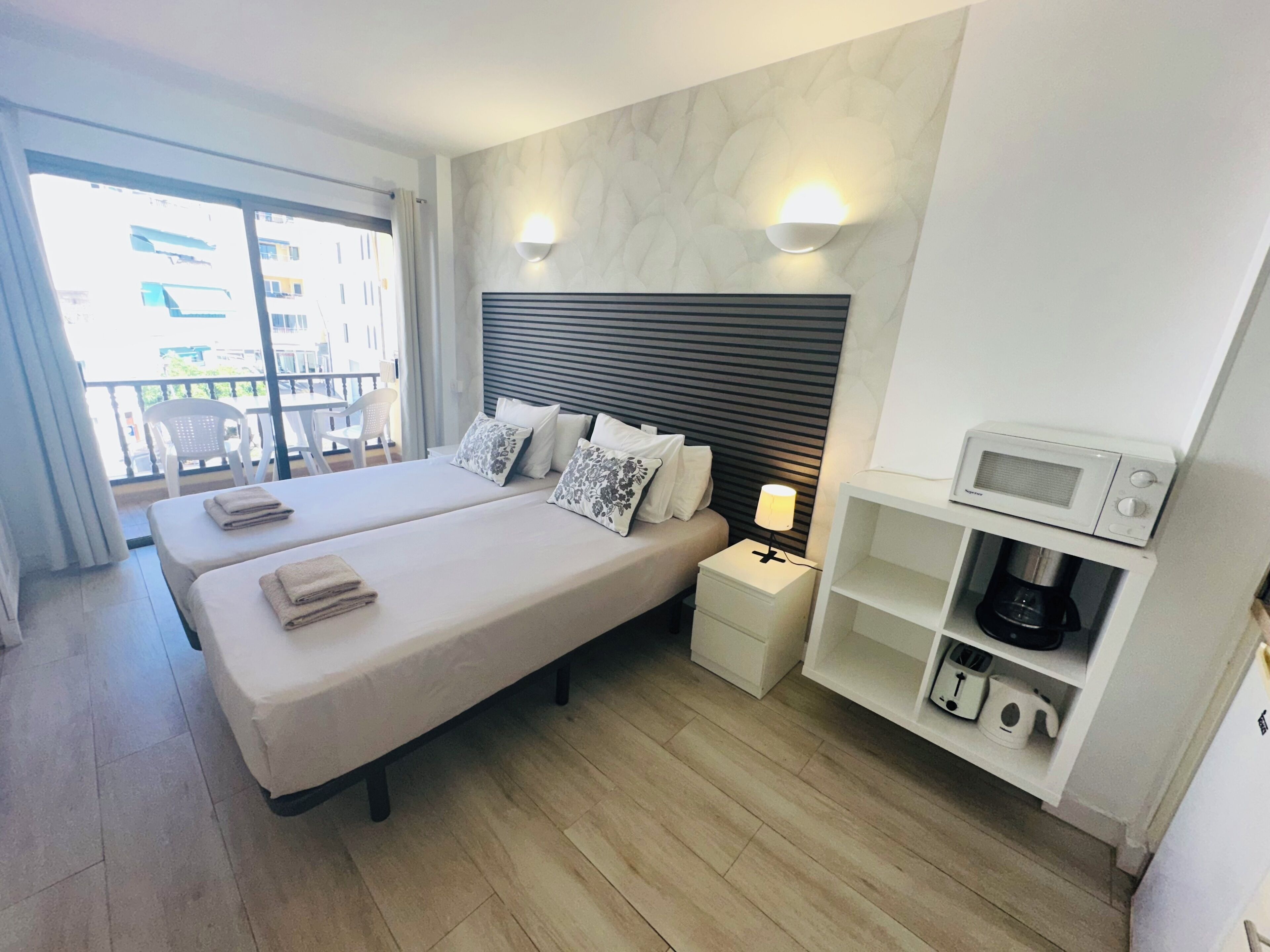A hotel room with two beds, a nightstand with a lamp, a microwave, and a coffee machine.
